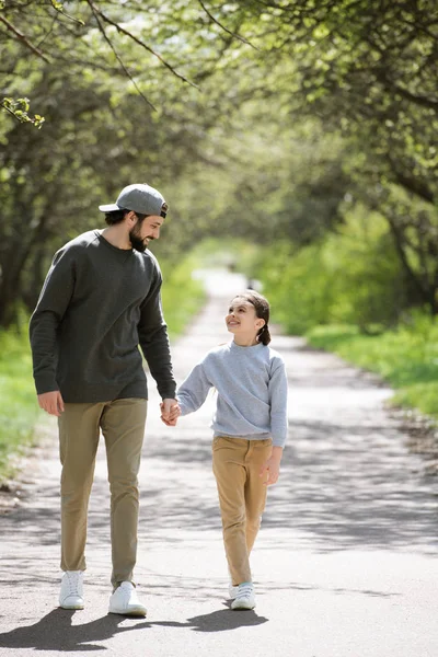 Усміхнений батько і дочка йдуть і тримають руки в парку — стокове фото