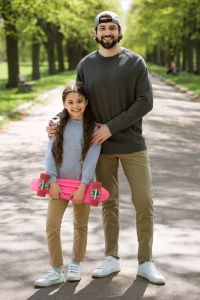 Hija con monopatín y padre en camino en el parque - foto de stock