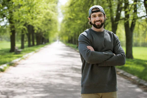 Uomo sorridente in piedi con le mani incrociate sul sentiero nel parco — Foto stock