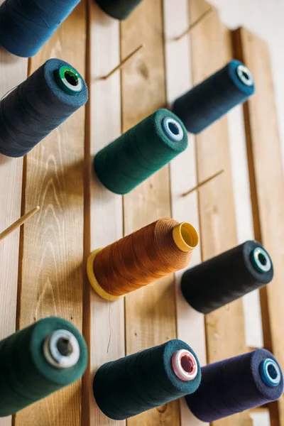 Colored thread coils hanging on wooden surface at sewing workshop — Stock Photo