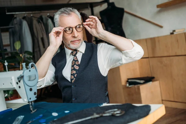 Старший портной носит очки для шитья в швейной мастерской — стоковое фото