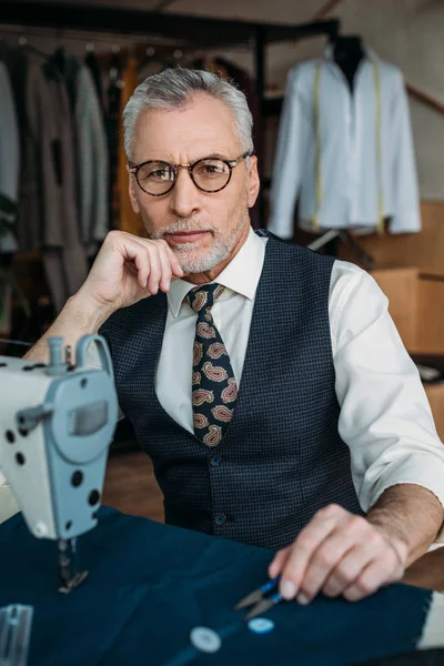 Handsome senior tailor looking at camera at sewing workshop — Stock Photo