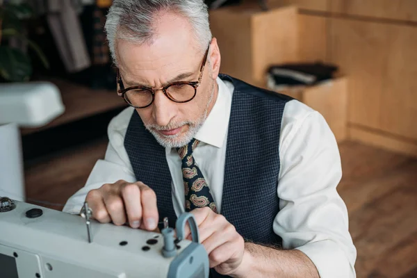 Senior tailor threading needle of sewing machine at sewing workshop — Stock Photo