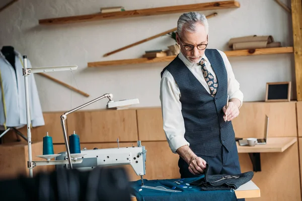 Tailleur senior examinant tissu à l'atelier de couture — Photo de stock
