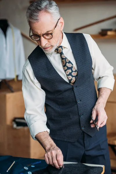 Tailleur de cheveux gris examinant tissu à l'atelier de couture — Photo de stock