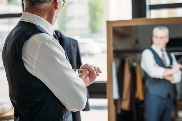 Tailleur senior debout devant le miroir à l'atelier de couture — Photo de stock