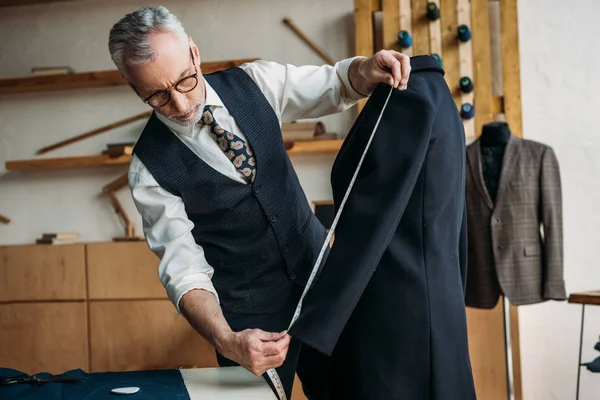 Seniorschneider messen Jackenärmel mit Maßband in Nähwerkstatt — Stockfoto