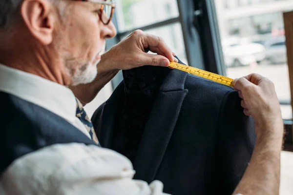 Side view of senior tailor measuring jacket with tape measure at sewing workshop — Stock Photo