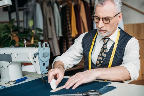 Senior tailor making pattern on cloth with piece of chalk at sewing workshop — Stock Photo