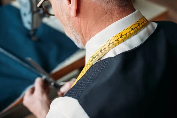 Image recadrée du tailleur senior coupant tissu foncé à l'atelier de couture — Photo de stock