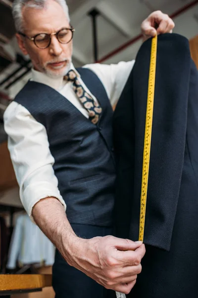 Senior tailor measuring sleeve of jacket with tape measure at sewing workshop — Stock Photo