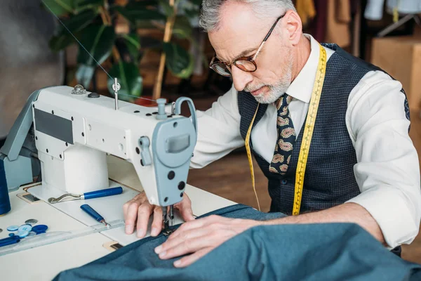 Beau tailleur dans des lunettes tissu à coudre avec machine à coudre à l'atelier de couture — Photo de stock