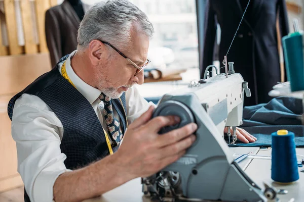 Side view of senior tailor sewing cloth with sewing machine at sewing workshop — Stock Photo