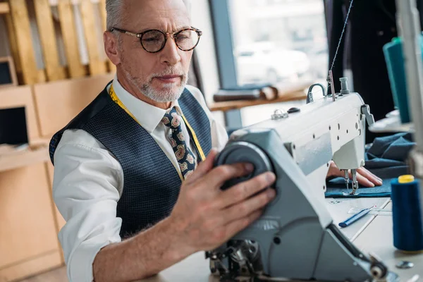 Handsome tailor sewing cloth with sewing machine at sewing workshop — Stock Photo