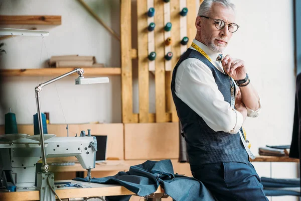 Bello sarto pensoso in piedi al laboratorio di cucito — Foto stock