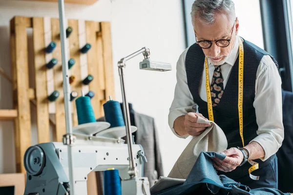 Handsome tailor choosing between dark and light clothes at sewing workshop — Stock Photo