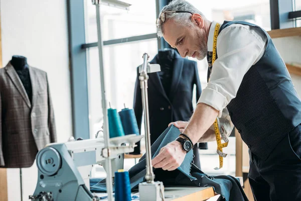 Bello sarto guardando panno a laboratorio di cucito — Foto stock