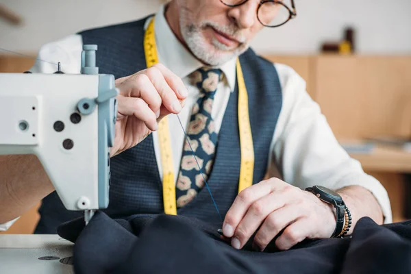 Cropped image of senior tailor sewing button to jacket at sewing workshop — Stock Photo