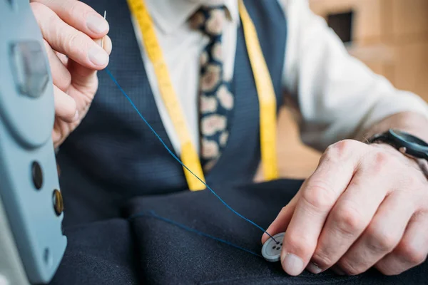 Cropped image of tailor sewing button to dark blue jacket at sewing workshop — Stock Photo