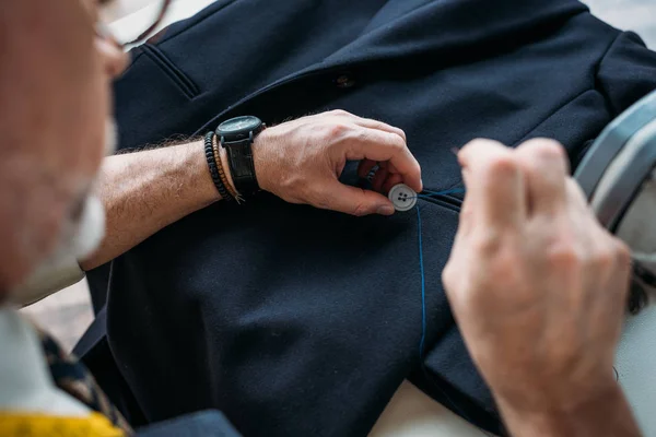 Cropped image of tailor sewing button to jacket at sewing workshop — Stock Photo