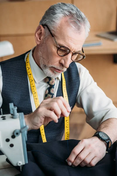 Handsome tailor sewing button to jacket at sewing workshop — Stock Photo
