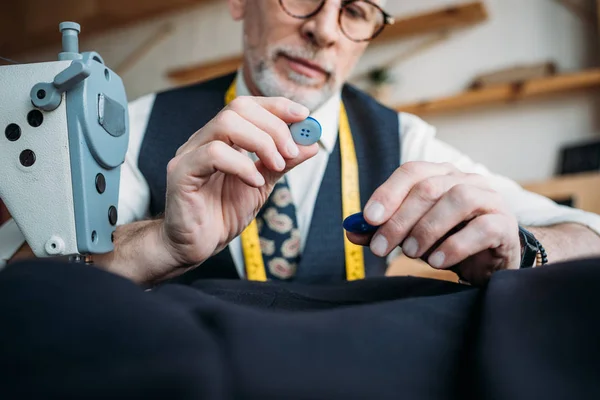 Imagen recortada del sastre guapo elegir botones en el taller de costura - foto de stock
