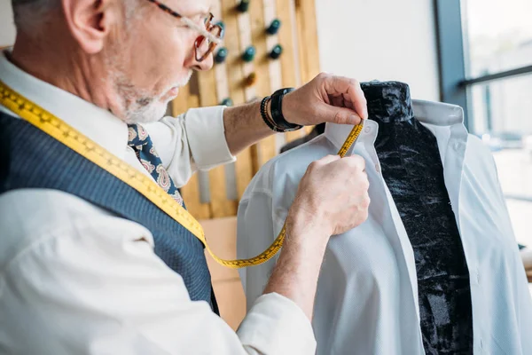 Handsome tailor measuring shirt with tape measure at sewing workshop — Stock Photo