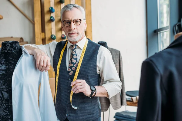 Beau tailleur appuyé sur le mannequin à l'atelier de couture et regardant la caméra — Photo de stock