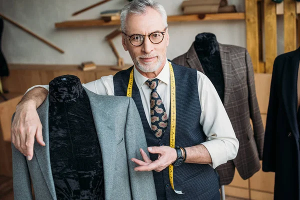 Handsome tailor showing jacket on mannequin at sewing workshop — Stock Photo