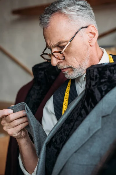 Serious mature tailor with measuring tape examining jacket on mannequin at sewing workshop — Stock Photo