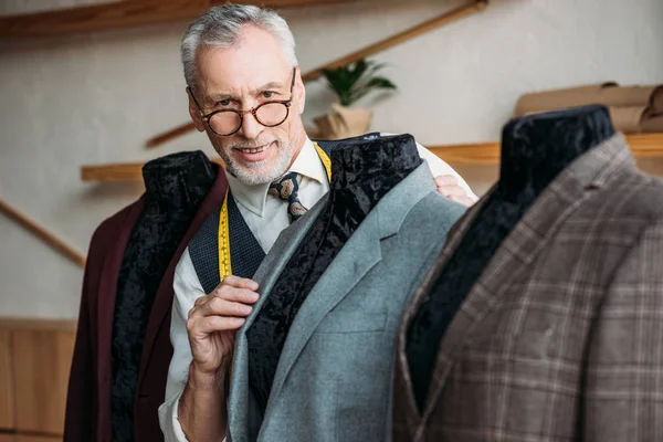 Lächelnde Schneiderin mit Maßband untersucht Jacke auf Schaufensterpuppe in Nähwerkstatt vor laufender Kamera — Stockfoto