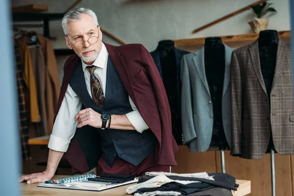 Schöne reife Schneiderin mit Jacke auf den Schultern am Arbeitsplatz in der Näherei — Stockfoto