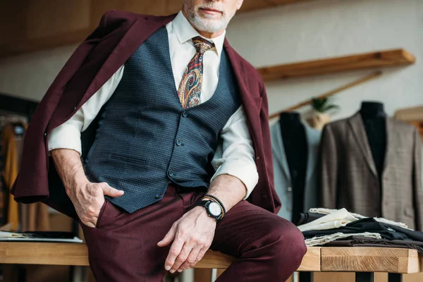 Cropped shot of mature man with jacket on shoulders sitting on table — Stock Photo