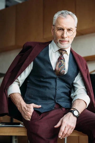 Handsome mature man with jacket on shoulders sitting on table — Stock Photo