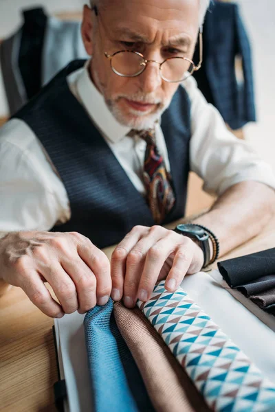 Stylish mature tailor looking at cloth samples at sewing workshop — Stock Photo