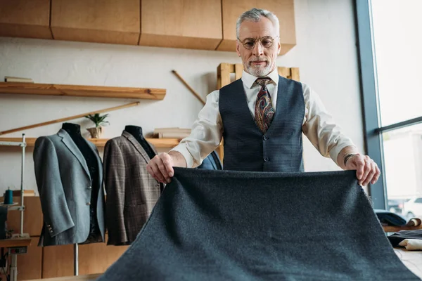 Tailleur mature sérieux avec tissu gris à l'atelier de couture — Photo de stock