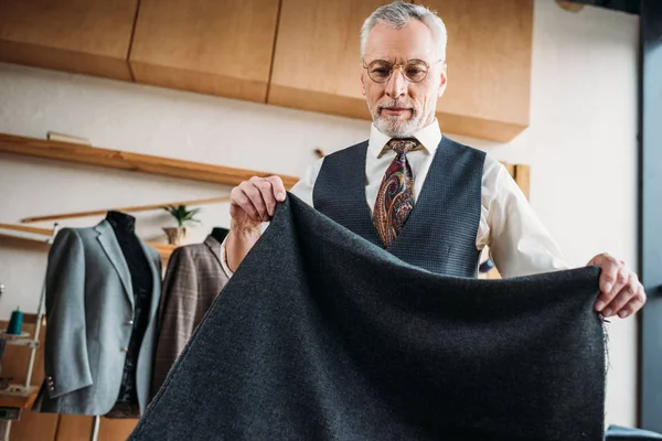 Bonito maduro alfaiate com cinza pano no costura oficina — Fotografia de Stock