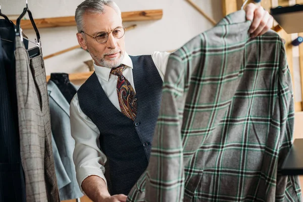 Grave maduro alfaiate examinando roupas na oficina de costura — Fotografia de Stock