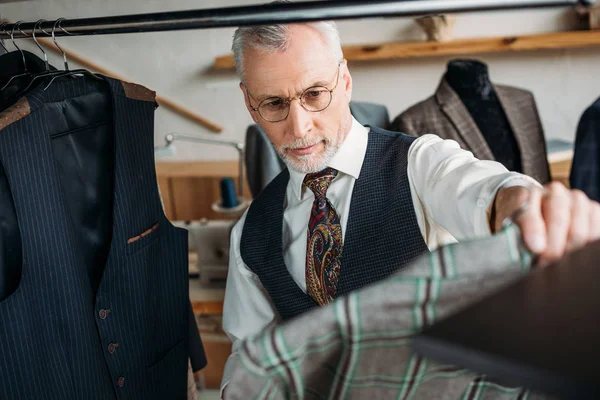 Уверенный зрелый портной осматривает одежду в швейной мастерской — стоковое фото