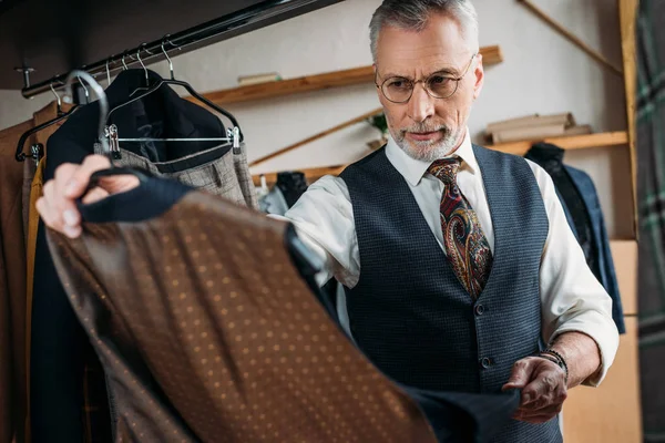 Bonito maduro alfaiate examinando roupas no costura oficina — Fotografia de Stock