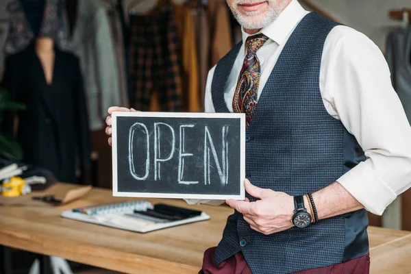 Cropped shot of tailor holding chalkboard with open sign at sewing workshop — Stock Photo