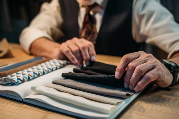 Cropped shot of tailor working with cloth samples at sewing workshop in late evening — Stock Photo