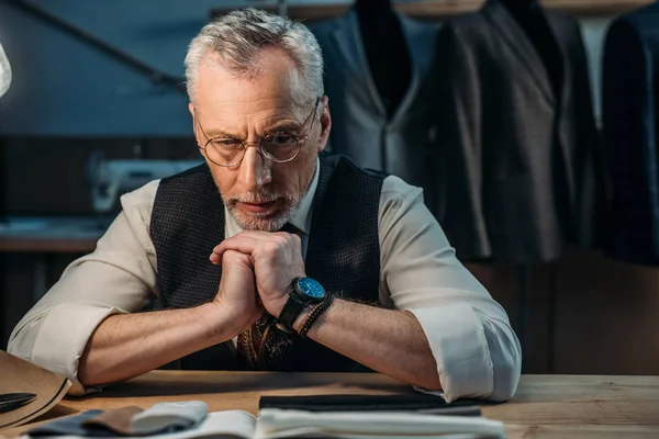 Premuroso sarto maturo guardando campioni di stoffa a laboratorio di cucito in tarda serata — Foto stock