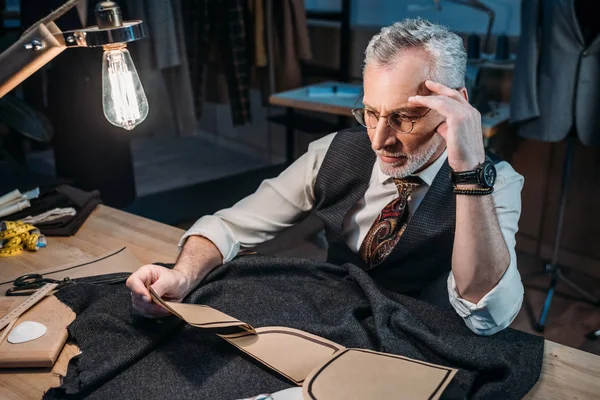 Thoughtful mature tailor sitting at workplace at sewing workshop in late evening — Stock Photo