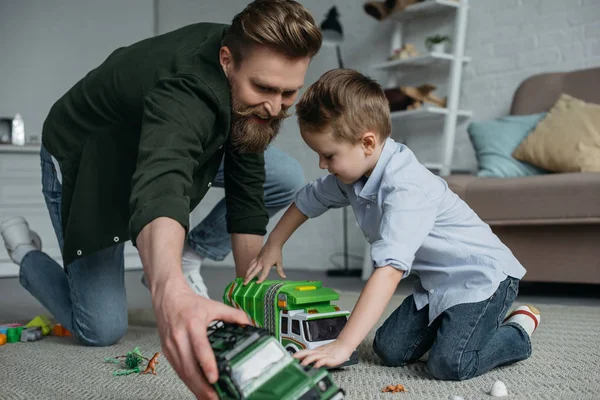 Sorrindo pai e filho brincando com carros de brinquedo juntos no chão em casa — Fotografia de Stock