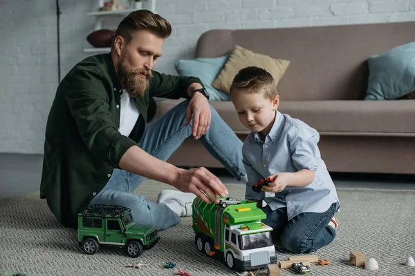 Padre e hijo pequeño jugando con coches de juguete juntos en el suelo en casa - foto de stock