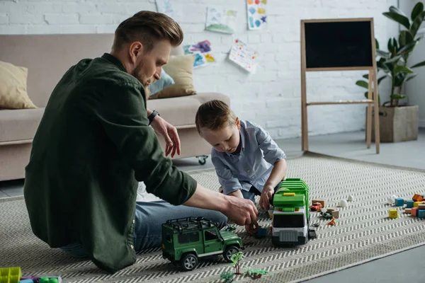 Vater und kleiner Sohn spielen zu Hause gemeinsam mit Spielzeugautos auf dem Boden — Stockfoto