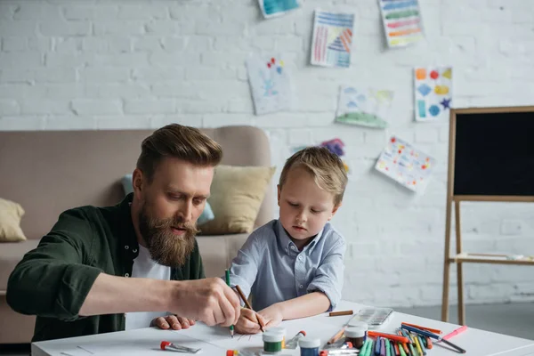Папа и милый маленький сын с красочными карандашами рисуют картинки вместе дома — стоковое фото