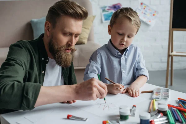 Батько і милий маленький син з барвистими олівцями малюють фотографії разом вдома — стокове фото