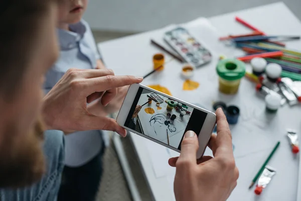 Partial view of man taking photo of sons picture on smartphone at home — Stock Photo